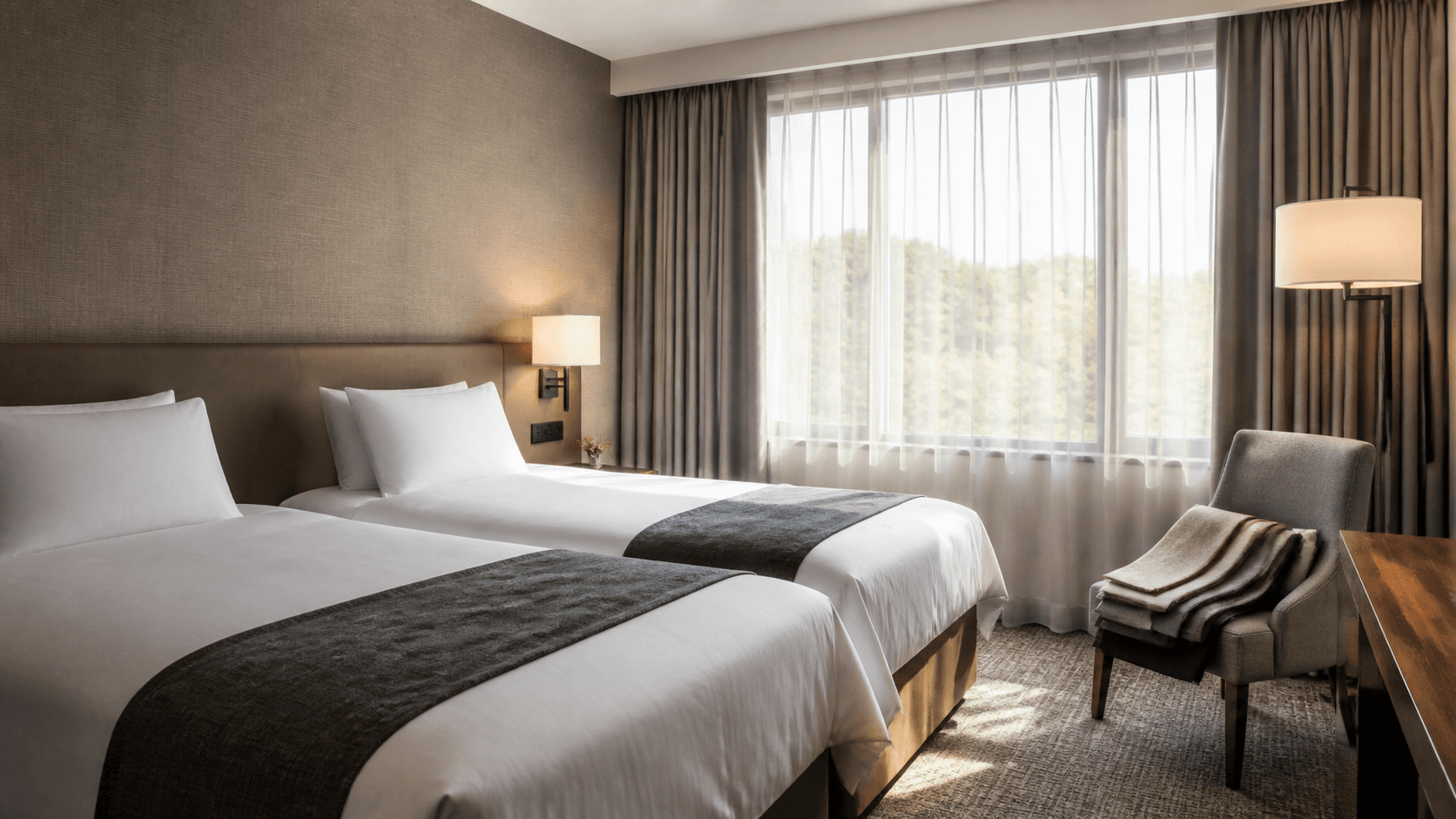Chambre de style hôtel avec deux lits blancs et linge neutre plié.
