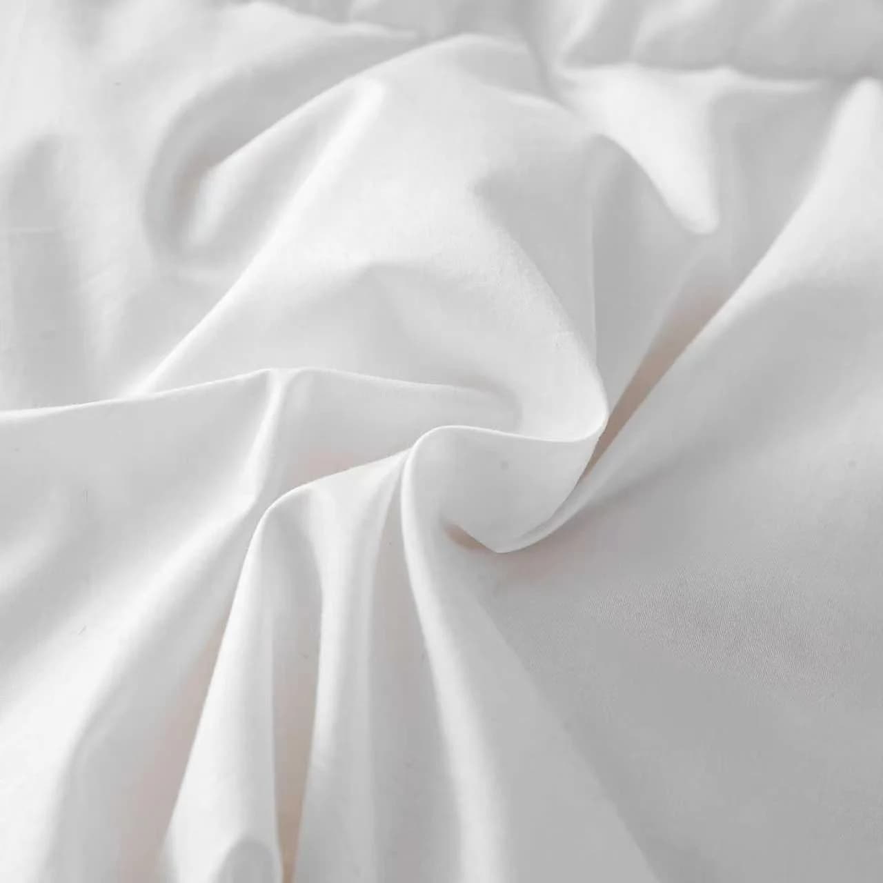 A close-up of crisp white cotton fabric arranged in a swirl of soft folds, showing a smooth matte surface and fine weave